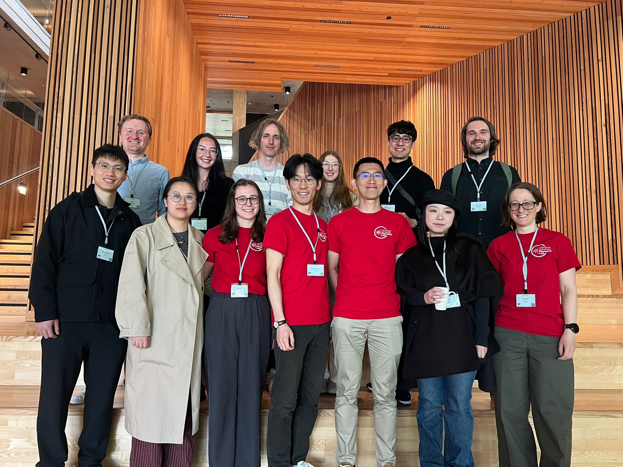 A group of 13 people standing in two rows, some sporting red Phonetics Lab T-shirts.